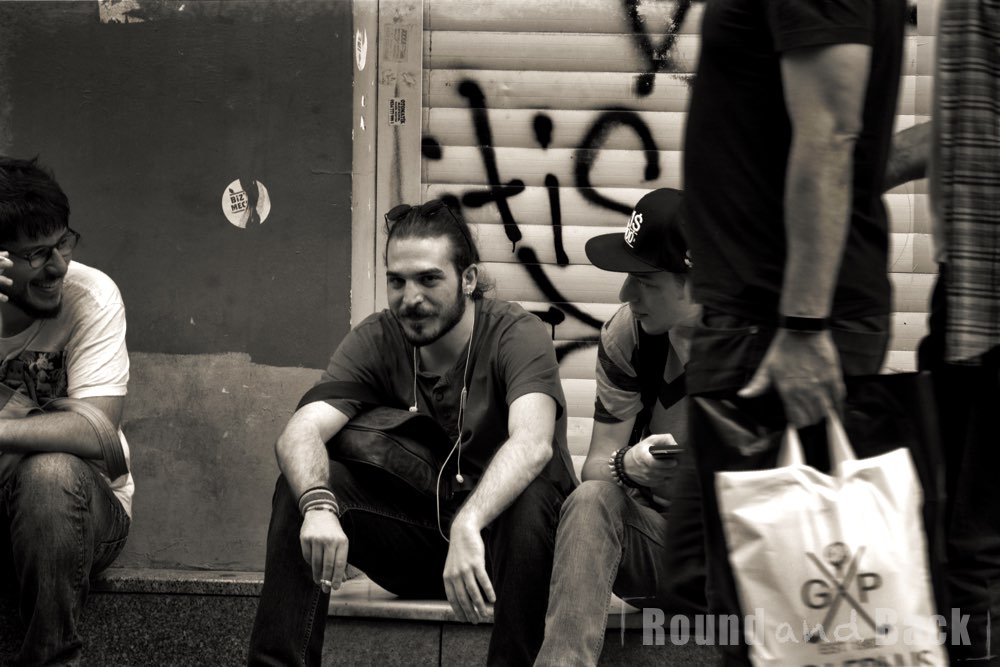 Junge erwachsene, die an einer Straßenseite sitze  und sich bei einer Zigarette unterhalten