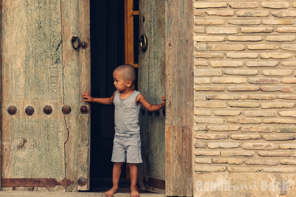 Kleiner Junger der vor den schweren Eingangstoren zu seinem Zuhause steht. Samarkand, Usbekistan.