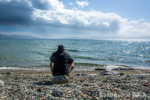 Caro die am Ufer des Song Kul sitzt während im Hintergrund ein paar Wolken aufziehen